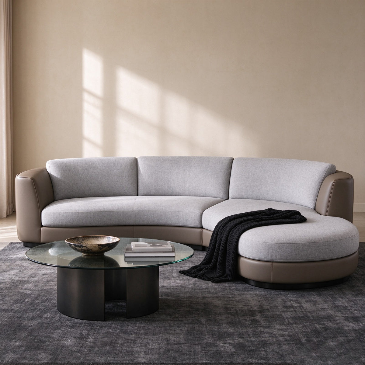 The sofa in a warm beige room with a glass and black coffee table, a knitted throw over the chaise and sunlight across the wall